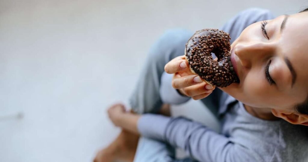 Pessoa segurando um doce em frente a uma balança, refletindo o equilíbrio entre desejos e saúde.