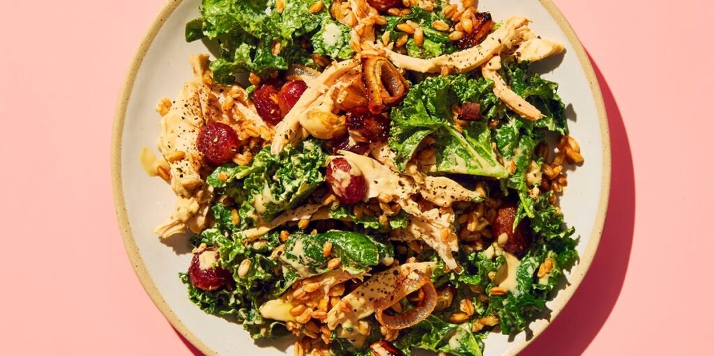 Salada saudável de couve com farro, frango desfiado e uvas roxas em uma tigela.