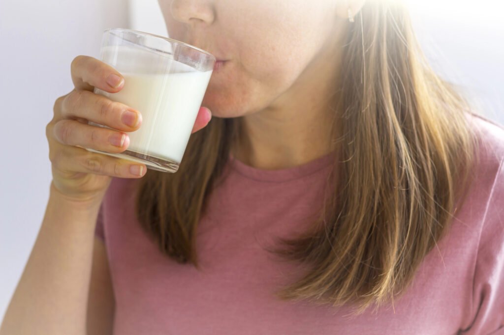 Imagem de um copo de leite ao lado de alimentos ricos em cálcio como brócolos e sardinhas.