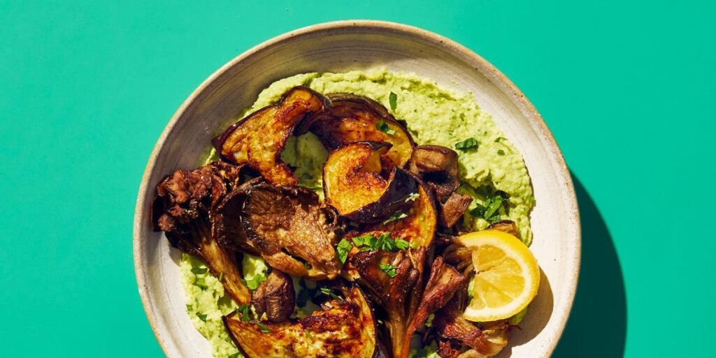 Hummus de alcachofra com berinjela temperada servido em um prato decorado com salsinha e fatias de limão.