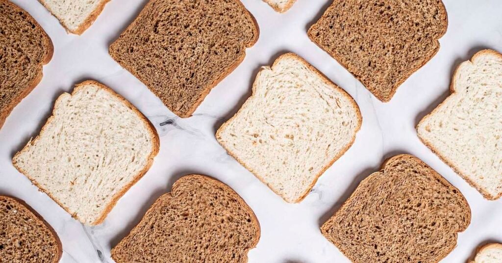 Alimentos ricos em carboidratos como pão integral, batata-doce e frutas, representando a energia necessária para treino.