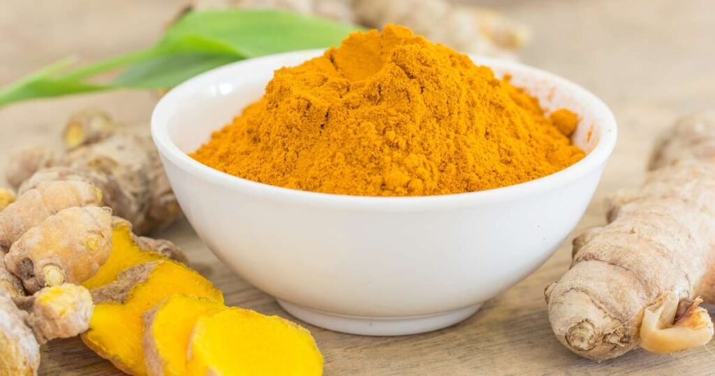 Raiz de cúrcuma fresca e cúrcuma em pó com pimenta-do-reino ao fundo