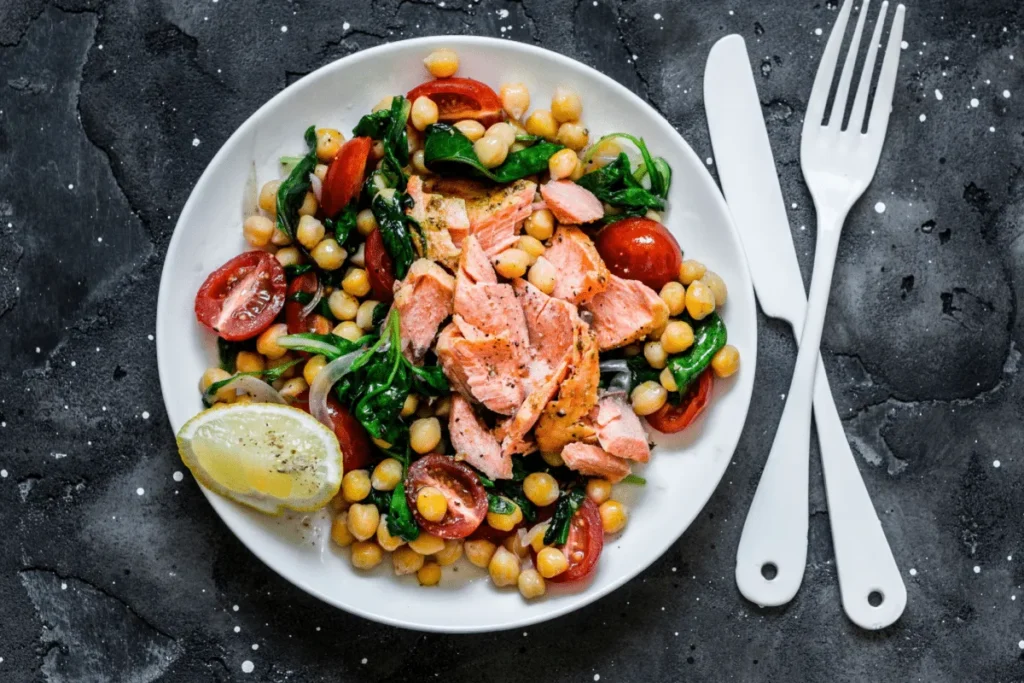 Salada morna de salmão com grão-de-bico e espinafre, rica em proteínas e apresentada em uma travessa.